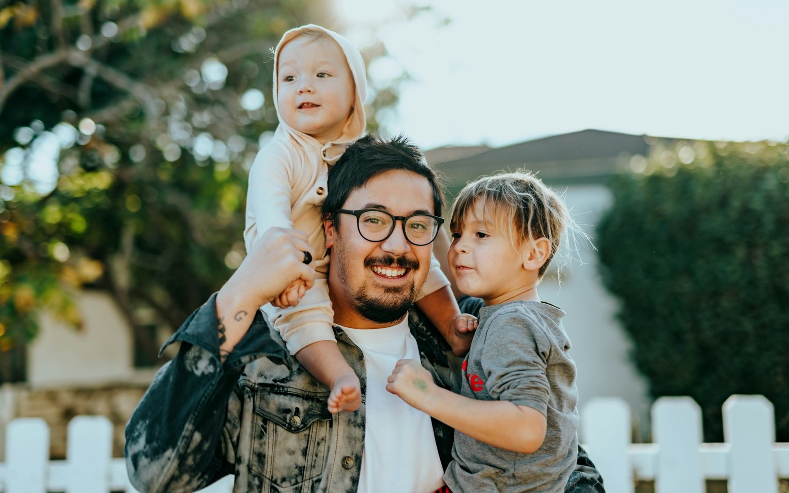 A father smiling outdoors with his two young children